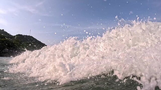 Waves crashing against rocks at shoreline in daytime near green hills