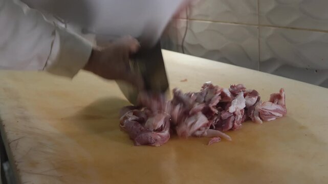 Close-up 10-bit slow motion of a chef hand-mincing lamb meat using a traditional satir cleaver on a wooden board. Initial stage of meat preparation for authentic Turkish kebabs.