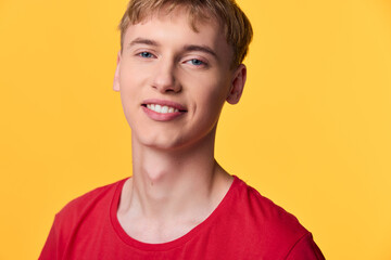 Young man with a bright smile in a red shirt poses casually against a vibrant yellow background, creating a friendly lifestyle image suitable for fashion, youth, and marketing