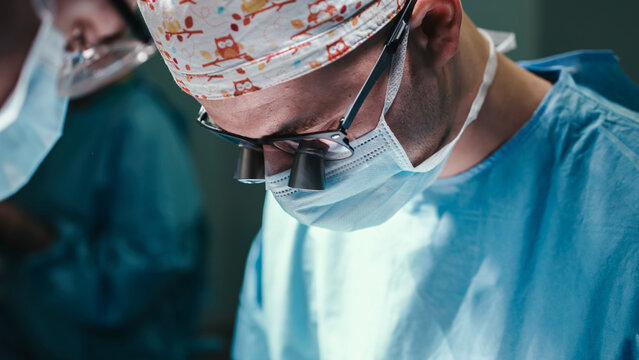Surgeon in operating room focused on procedure, wearing surgical mask and cap, illuminated by bright lights, showcasing dedication and precision in medical practice