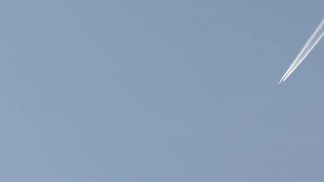 High altitude jet plane flying across a clear blue sky leaving white contrails behind. Concept of travel, air transportation, and freedom in the vast atmosphere.

