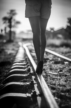 Woman walking on railway track balancing in high heels, concept of risk, uncertainly and life journey in black and white
