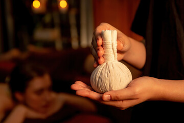 Hot herbal ball spa massage body treatment with masseur's hand hold or show herb bag at spa. Tranquil and serenity of aromatherapy recreation in warm lighting of candles at spa salon. Quiescent © InfiniteFlow