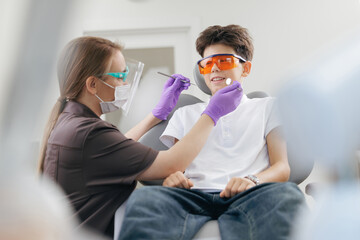 Dentistry clinic doctor examines boys teeth, caucasian male child at dentist wearing protective UV...