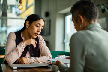 Adult businesswoman discussing paperwork with mature colleague in office, thoughtful