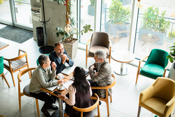 Adult and senior colleagues having friendly business meeting in modern cafe