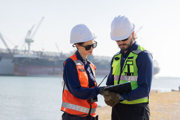 Workers discuss plans at a port with a cargo ship in the background