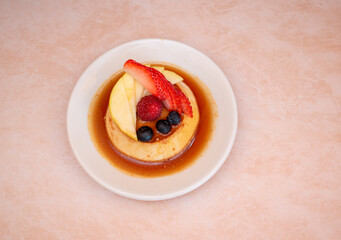 Imagen horizontal y cenital de un plato blanco de un postre llamado flan napolitano cocn frutos rojos 