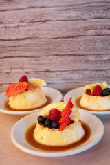 Imagen vertical de tres platos de flan napolitano con caramelo y frutos rojos con fondo de madera