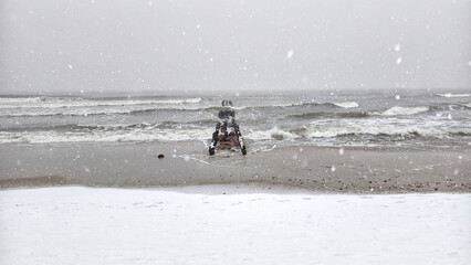 A winter snowstorm on Zelenogradsk's Baltic beach: swirling snow and crashing waves erode the icy sand around the crumbling wooden breakwaters. 