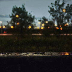 photo depicting rainy evening scenery, in the foreground raindrops, in the background blurred silhouettes of trees and lanterns