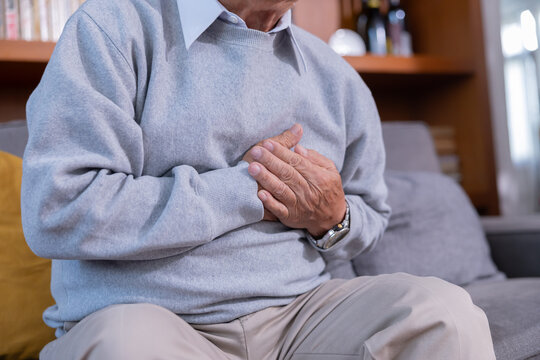 Elderly man grab his chest with hand suffer from chest pain in a living room