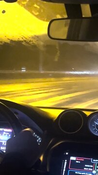 Vertical video of a man driving a car at night, seen from behind, on a rainy day along a highway. Interior view with a slightly fogged windshield