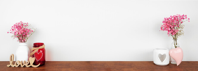 Valentines Day love and heart theme home decor and flowers on a wooden shelf against a white wall. Copy space.