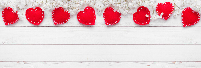 Valentines Day top border of cloth hearts and white flowers. Above view on a white wood banner background. Copy space.