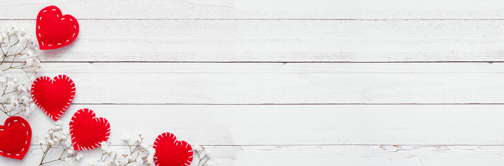 Valentines Day corner border of cloth hearts and white flowers. Top down view on a white wood banner background. Copy space.
