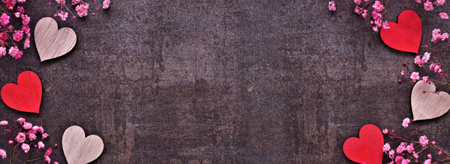 Valentines Day double border of wooden hearts and pink flowers. Top down view on a dark banner background. Copy space.
