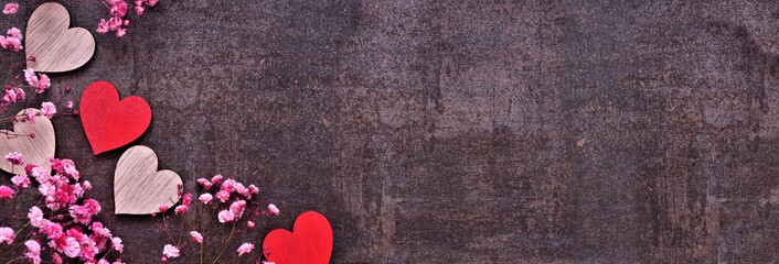 Valentines Day corner border of wooden hearts and pink flowers. Above view on a dark banner background. Copy space.
