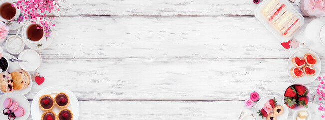 Valentines Day or love theme afternoon tea. Above view double border against a white wood banner background. Variety of finger sandwiches, sweet desserts and pastries. Copy space.