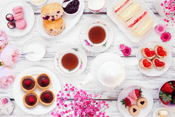 Valentines Day or love theme afternoon tea. Overhead view table scene against a white wood background. Assortment of finger sandwiches, sweet desserts and pastries.