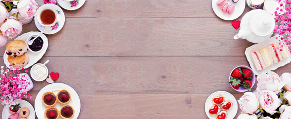 Valentines Day or love theme afternoon tea. Above view double border against a wood banner background. Variety of finger sandwiches, sweet desserts and pastries. Copy space.