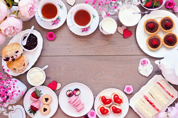 Valentines Day or love theme afternoon tea. Above view frame against a wood background. Variety of finger sandwiches, sweet desserts and pastries. Copy space.