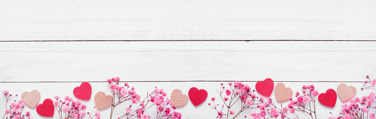 Valentines Day bottom border of wood hearts and pink flowers. Top view on a white wood banner background. Copy space.