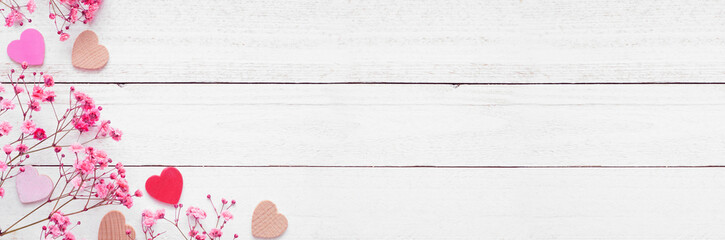 Valentines Day corner border of wood hearts and pink flowers. Top down view on a white wood banner background. Copy space.