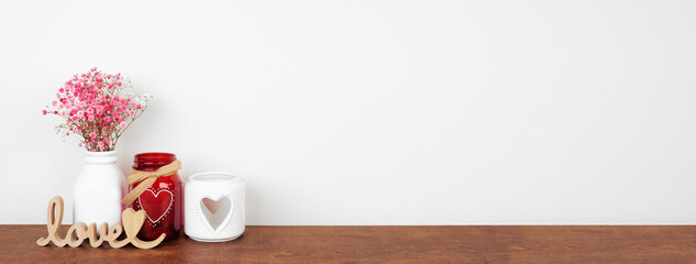 Valentines Day love and heart theme home decor and flowers on a wood shelf against a white wall. Copy space.