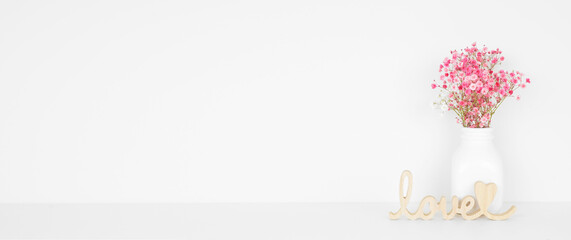 Valentines Day home decor and flowers on a white shelf against a white wall. Wooden love sign and pink baby's breath. Copy space.