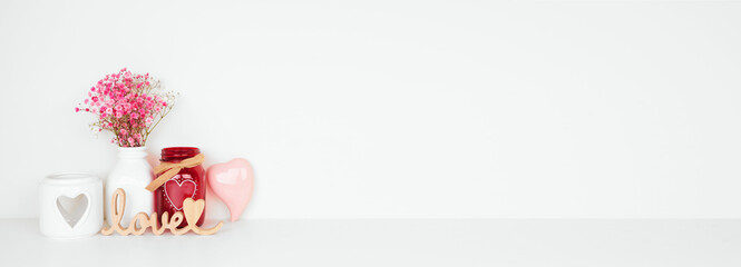 Valentines Day love and heart theme home decor and flowers on a white shelf against a white wall. Copy space.