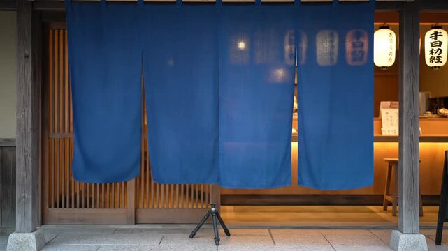 Traditional Japanese Noren Curtain Entrance to a Cozy Restaurant at Dusk Illuminated by Soft Lantern Light Featuring Wooden Architecture and Stone Pavement in Kyoto Japan