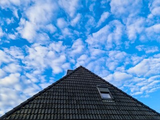 Fototapeta premium Dark tiled roof against blue sky with white clouds