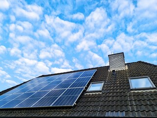 Fototapeta premium Solar panels generating clean energy on house roof under blue sky