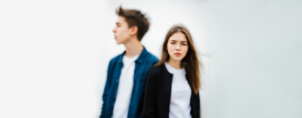 teenage girl looking worried and serious while a teenage boy stands blurred in the background looking away suggesting social distance