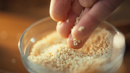 A man's hands carefully cradle sesame grains, checking their quality as they fall and pour into a bowl, assessing the harvest's quality and freshness in a traditional process