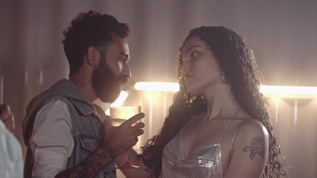 Young attractive couple flirting and dancing at a nightclub party with warm atmospheric lighting and haze.