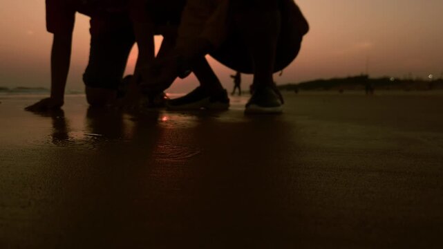 Children playing on sea beach sand at sundown beneath an amber sky and dramatic sunset background, with soft light and colorful horizon reflecting a peaceful nature and landscape evening scene.