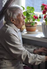 Old lonely woman sitting near the window in his house.