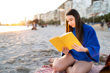 Young girl enjoying peaceful moment reading book on sandy beach