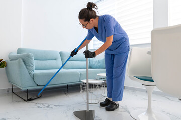 Professional cleaning woman sweeping a bright, modern office waiting room floor, maintaining hygiene and order with a broom and dustpan in a clean environment