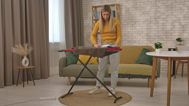 A young woman uses a lint roller to remove lint and hair from a sweater while washing it in her cozy home.