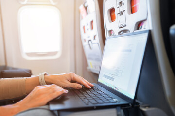 Female working on laptop during flight inside airplane cabin. Business travel and digital nomad lifestyle concept, transportation and remote productivity