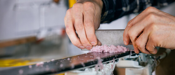 Ski maintenance and repair. Closeup of service worker scraping dry wax off ski base. copy space