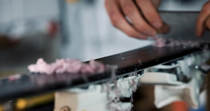 Ski maintenance and repair. Closeup of service worker scraping dry wax off ski base