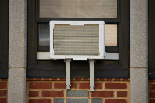 external view of a window air conditioner unit with an adjustable window support mounting bracket in a red brick building