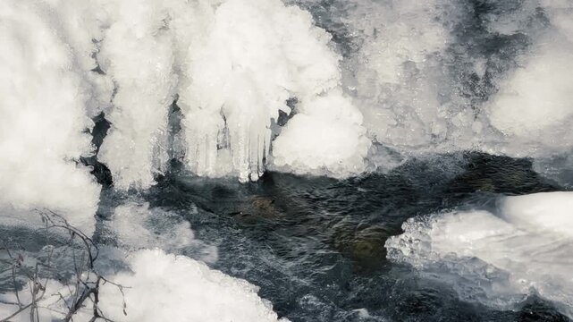 Clean river water flowing during sunny winter day with foamy waves. Ice in the water. Snowy river and nature concept.