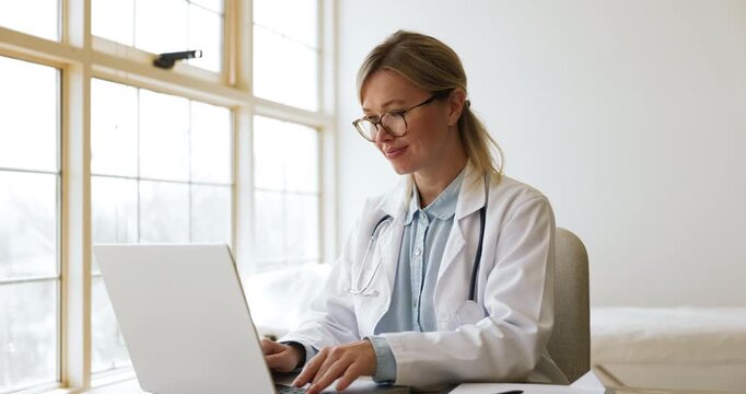 Thoughtful female GP doctor in uniform working on laptop, thinking disease diagnosis, reviewing patient diagnose, evaluating health test results, doing medical research, deciding best treatment plan
