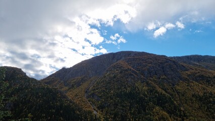 Majestic mountains under a blue sky with scattered clouds and autumn trees