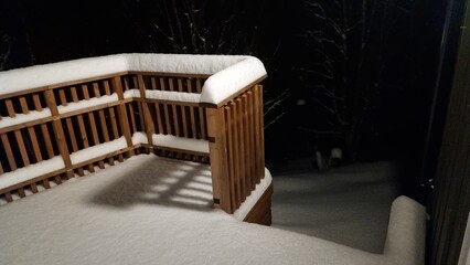 Snow covers wooden deck at night showing quiet winter scene with trees in background and fresh snowfall on ground